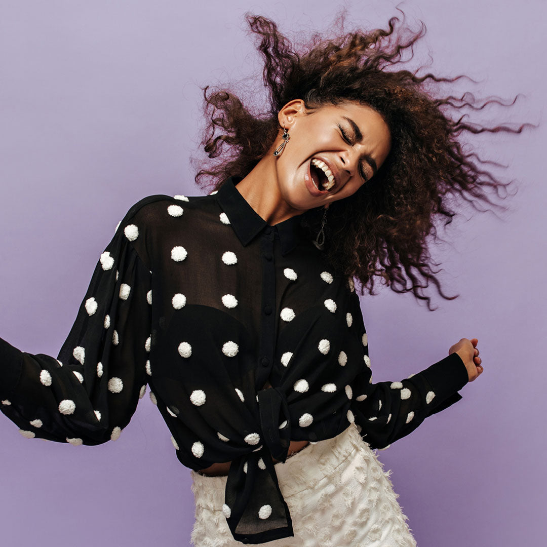 Happy fashionable woman wearing a black top with white polka dots and white pants.